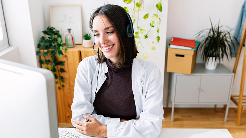 Portrait of young female doctor in headset working at consultation room listening patient through online virtual meeting video call. Medicine assistance concept.