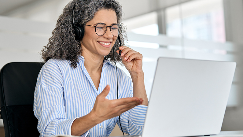 Happy mature business woman call centre representative customer support agent talking to client, smiling middle aged senior female operator wearing headset working using laptop computer in office.