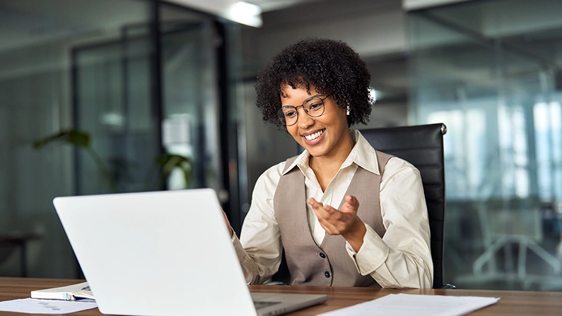 Happy professional young African female hr manager, smiling business woman in office wearing earbuds looking at laptop computer having hybrid conference work meeting or remote job interview.