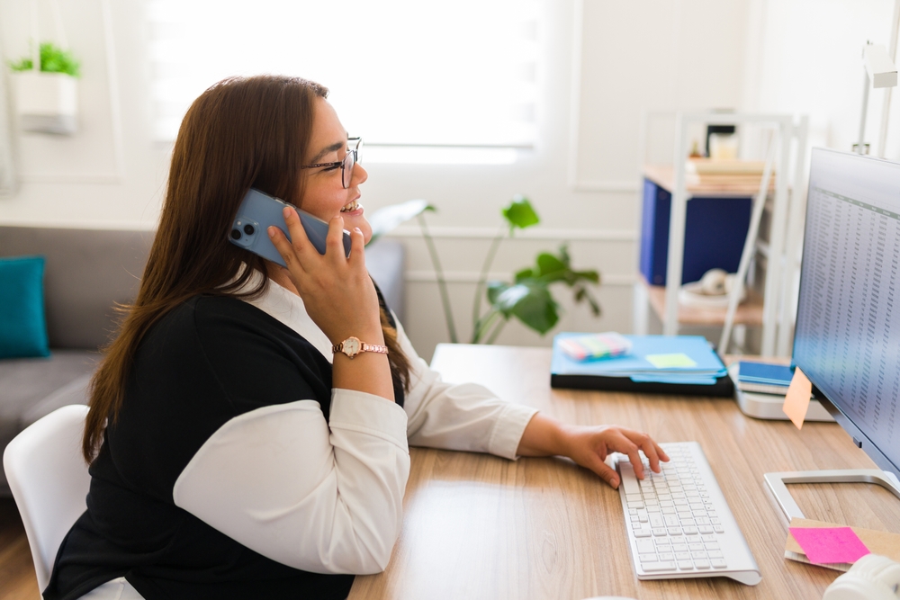 woman working as an accountant and typing on the computer at her office while talking on the phone