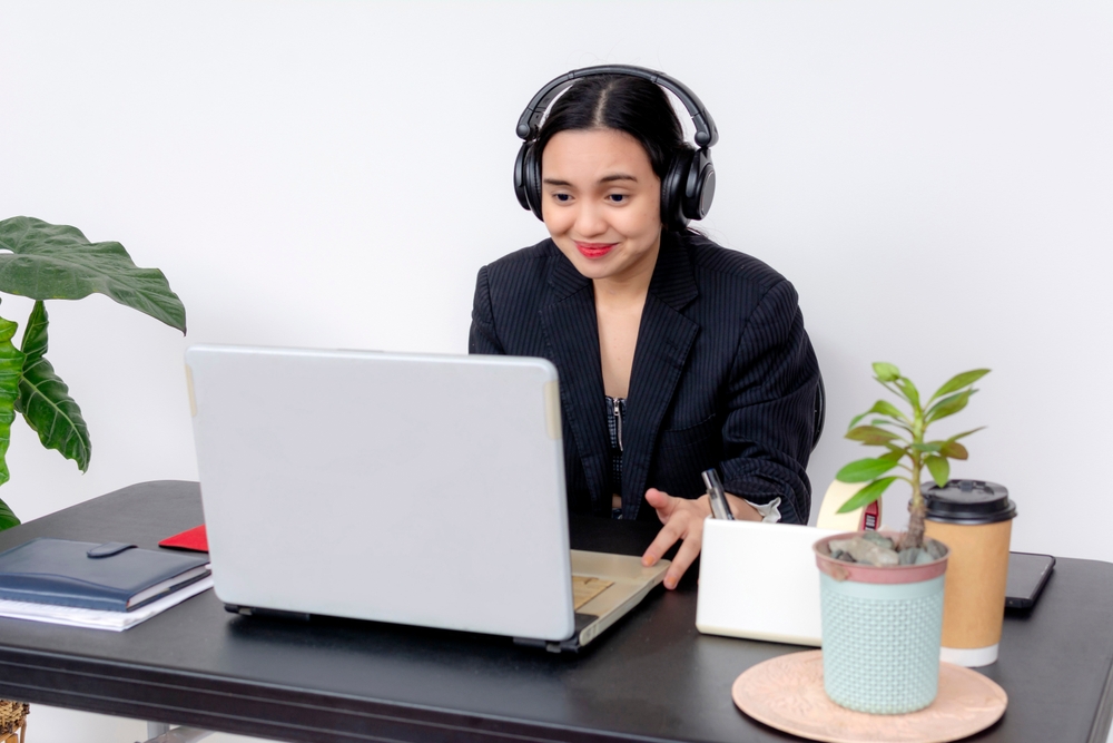 A professional female call center agent wearing headphones, working at her desk with a laptop