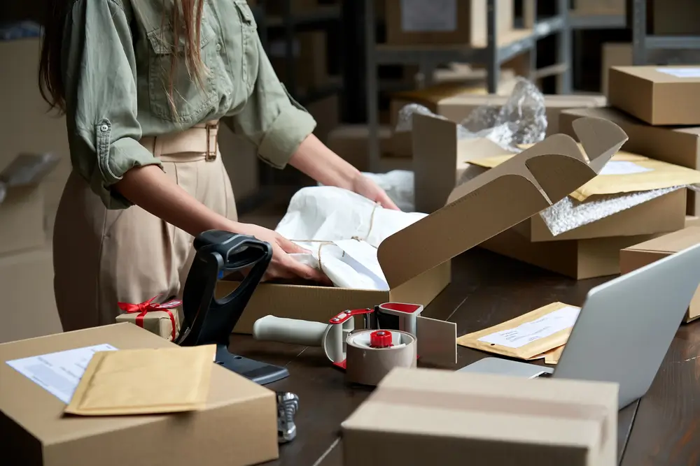 Closeup view of female online store small business owner seller entrepreneur packing package post shipping box preparing delivery parcel on table.