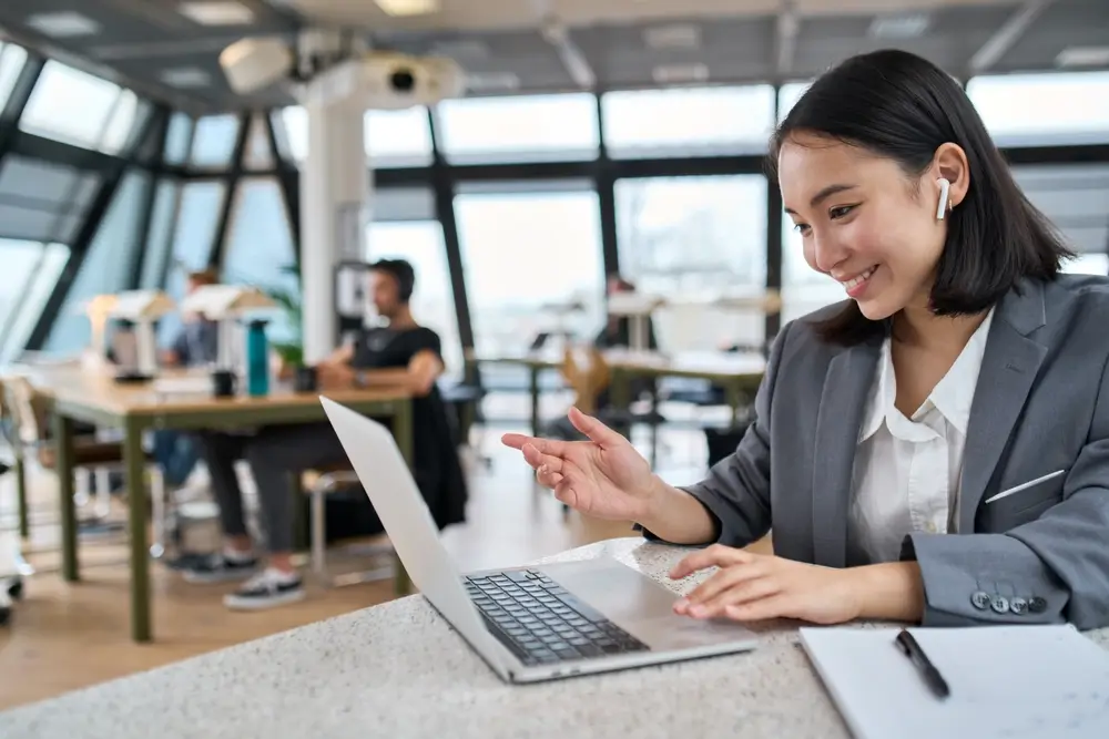 Young Asian business woman employee or executive manager using computer looking at laptop and talking leading hybrid conference remote video call virtual meeting or online training working in office.