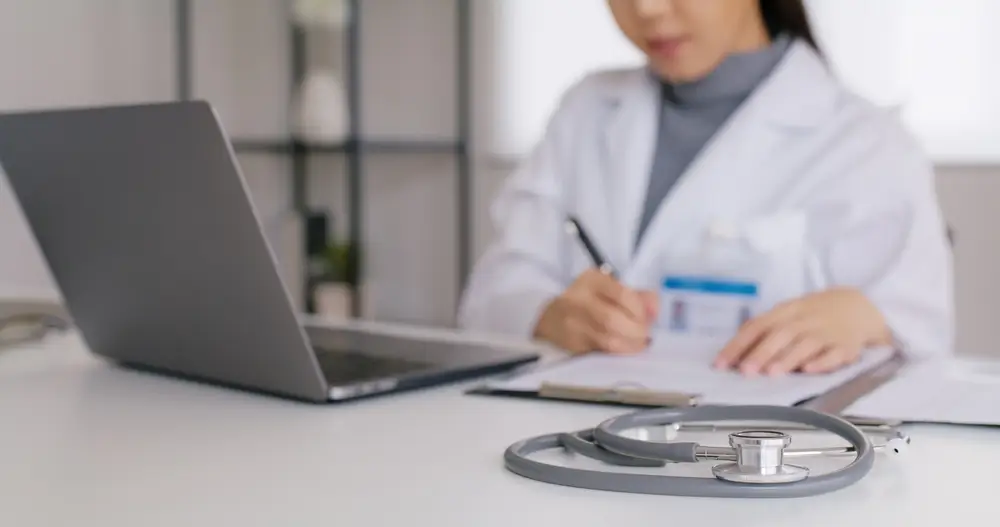 healthcare virtual assistant in a meeting on laptop and taking down notes.