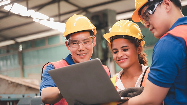 A diverse team of construction workers reviewing plans on a laptop, showcasing remote construction management in action.