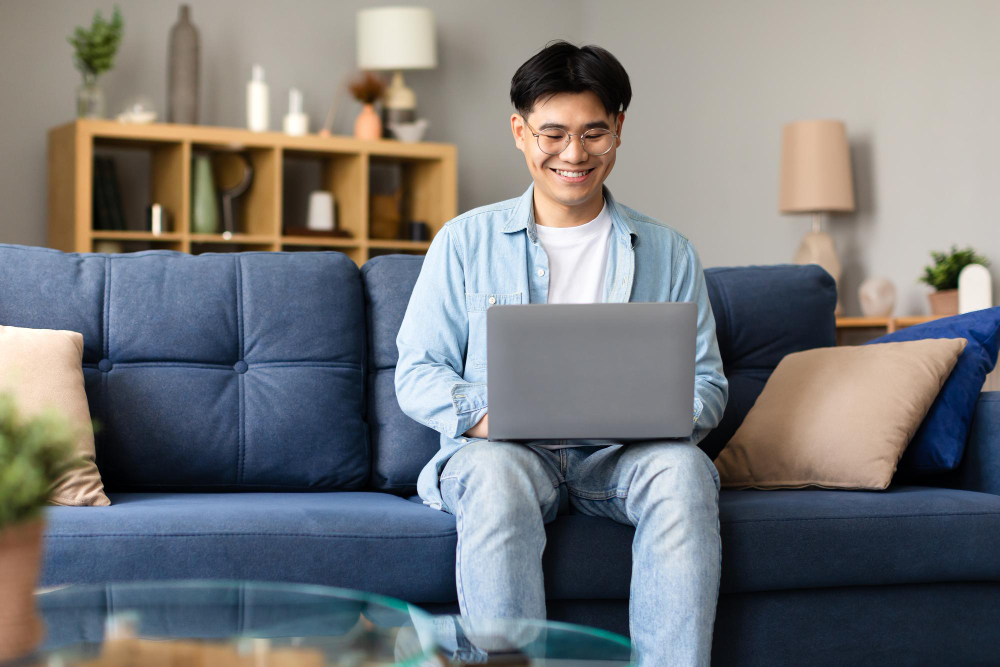 Asian freelancer guy sitting with laptop working online at home