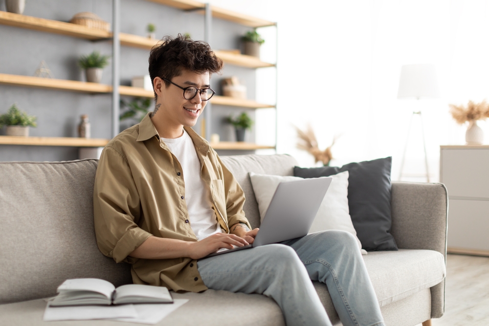 Young guy using laptop sitting on sofa in living room
