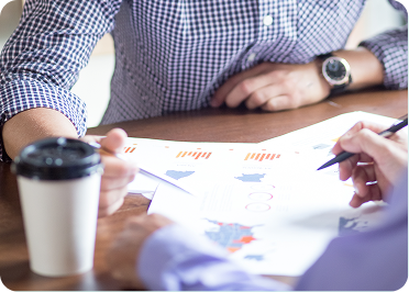 Two people sit at a table with a cup of coffee and a pen, engaged in conversation or collaboration.