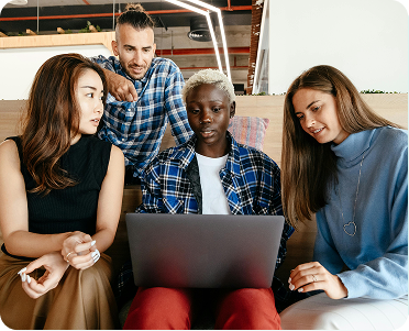 A group of four people sitting on a couch, focused on a laptop screen in a cozy living room setting.