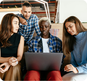 A group of four people sitting on a couch, focused on a laptop screen in a cozy living room setting.