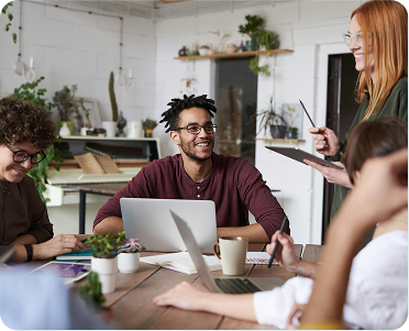 A diverse group of people collaborating around a table, each using a laptop for discussion and teamwork.