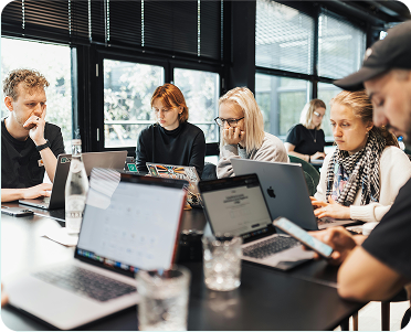 A group of diverse individuals seated at a table, each using a laptop for collaborative work.