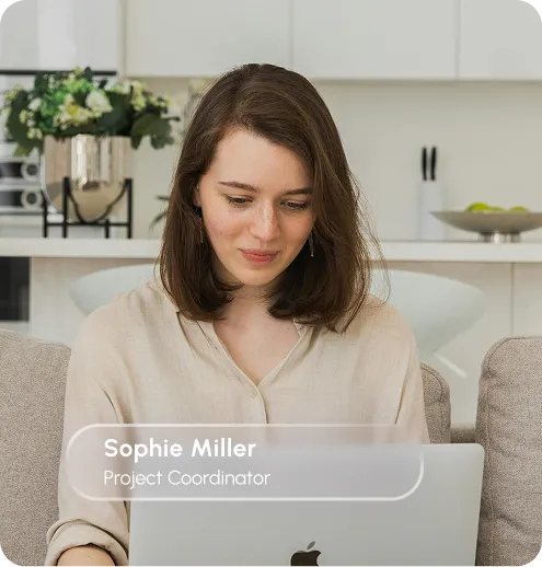 A woman sitting on a couch, focused on her laptop, with a cozy living room setting in the background.