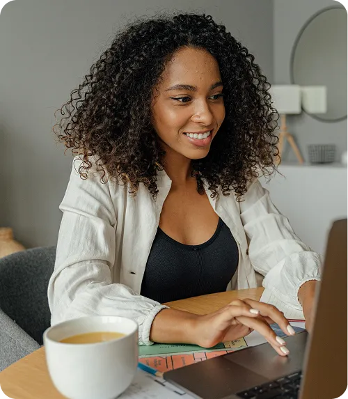 A woman smiles while working on a laptop, conveying a sense of joy and engagement in her task.