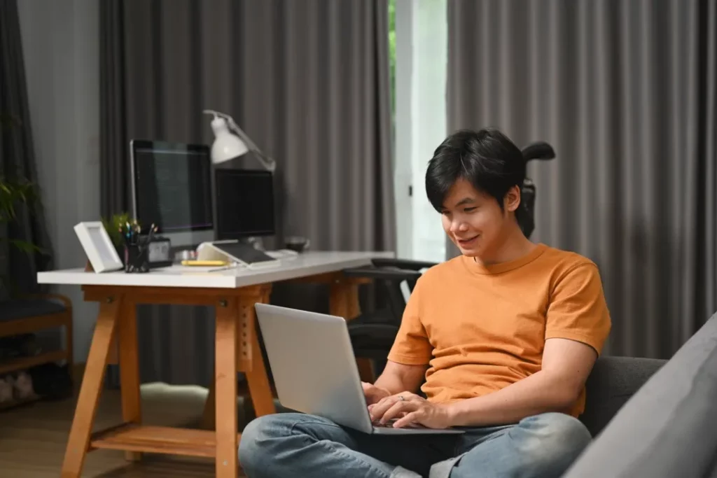 Happy casual man freelancer using laptop while sitting on sofa