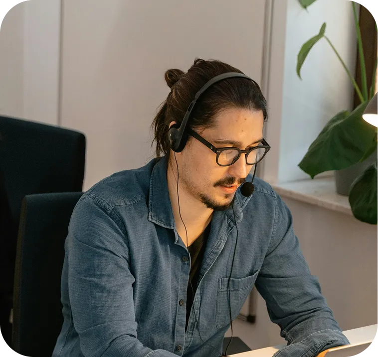 A man wearing headphones sits at a desk, focused on his work with a computer in front of him.
