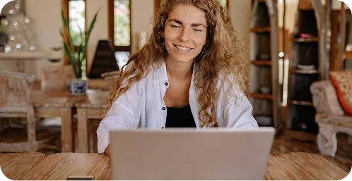 A woman smiles while working on a laptop, conveying a sense of joy and engagement with her task.