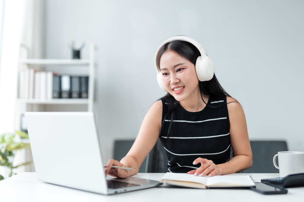 Happy virtual assistant wearing headphones is using laptop for work