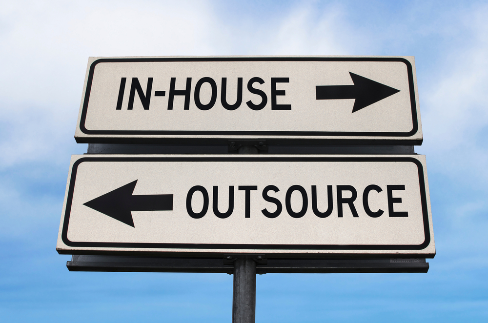 Outsource versus in-house road sign with two arrows on blue sky background.