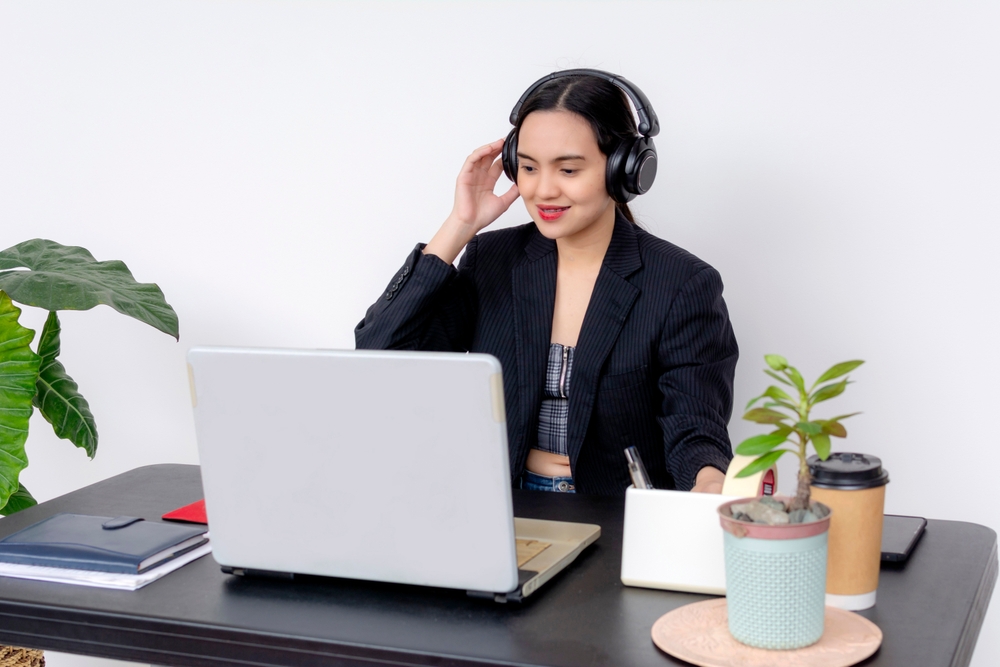 A professional female call center agent wearing headphones, working at her desk with a laptop in casual modern attire.
